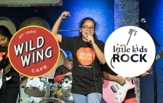 Student band performing onstage with the Wild Wings Cafe and Music Will logos on top.