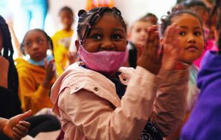 Children in masks are excited and clapping during an instrument delivery.