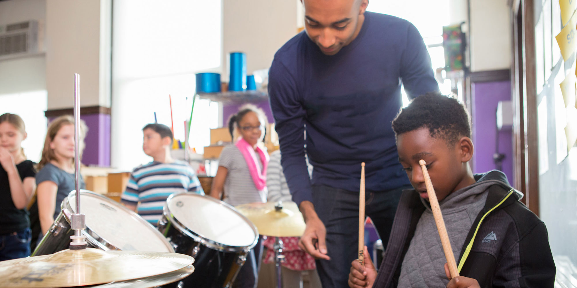 boy-playing-drums-with-teacher-behind-him